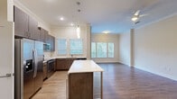 This single-floor residence offers a thoughtfully designed layout across four bedrooms and two bathrooms. The open-concept kitchen and living area serves as the heart of the home, featuring rich dark-walnut cabinetry extending to the ceiling, a white quartz-topped island with pendant lighting, and a full suite of stainless steel appliances including a French door refrigerator, range, microwave, and dishwasher. Wood-look flooring runs throughout this shared space, and multiple windows with horizontal blinds allow generous natural light while offering views of surrounding greenery. Crown molding and a ceiling fan add refined detail to the living area.

The bedrooms are carpeted for comfort; the generously sized primary bedroom includes a walk-in closet with built-in shelving and two windows. Additional bedrooms offer similar neutral tones, hard-surface or carpeted flooring, and crown molding details. Two hallways connect the rooms efficiently throughout the unit.

The bathrooms are finished with large-format marble-look tile. One features a walk-in shower with a framed glass door, while the second includes a soaking tub and tiled shower surround, both appointed with brushed nickel fixtures. Overall, the space presents a clean, contemporary aesthetic with consistent, quality finishes.