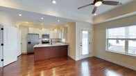 This well-appointed single-floor residence offers two bedrooms and one bathroom across a generously sized layout. The open-concept design connects the kitchen and living area seamlessly, creating an inviting and functional space. The kitchen is a standout feature, outfitted with white cabinetry, granite countertops, and a rich dark-wood island that provides both additional prep space and casual seating. Stainless steel appliances, including a refrigerator, range, and microwave, complete the modern kitchen setup. Recessed lighting throughout ensures bright, even illumination, while crown molding adds a refined architectural touch to the tray ceilings. Warm hardwood floors extend across the main living area, contributing to a cohesive and polished aesthetic. A ceiling fan in the living space enhances comfort, and a glass-paned door allows natural light to filter in while providing access to the outdoors. The neutral wall tones create a versatile backdrop that complements a variety of décor styles. Overall, this residence balances practical design with thoughtful finishes, making it a comfortable and attractive living space.