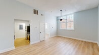 Located at 2132–2144 Park St in Columbia, SC, this 1-bedroom, 1-bathroom residence offers a clean, modern aesthetic throughout. Light blue-gray walls and warm light wood-tone flooring run consistently across every room, creating a cohesive and inviting atmosphere.

The open living area benefits from soaring ceilings and a large multi-pane window that draws in generous natural light, complemented by a sleek ceiling fan with a matte black finish. A charming entry door with transom window detail adds architectural character to the space.

The galley-style kitchen is well-equipped with white shaker cabinetry, matte black hardware, a marble-look quartz countertop, a stainless steel undermount sink with a black gooseneck faucet, and a full suite of stainless steel appliances including a refrigerator, range, and over-the-range microwave.

The bedroom is generously sized, featuring multiple windows that frame views of surrounding brick architecture and allow for abundant natural light, along with a ceiling fan and closet access.

The bathroom is finished with white shaker-style cabinetry, a quartz countertop, matte black fixtures, and a full tub-shower combination with clean white surround. Light wood flooring continues seamlessly into the bathroom, tying the overall design together.