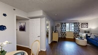 This single-floor residence offers a thoughtfully designed layout that connects each living area with a consistent and cohesive aesthetic. Rich dark hardwood flooring flows throughout, complementing the soft grey walls and accents of navy blue found across the space.

The living room is a comfortable and well-lit gathering area, featuring a large window dressed with bold ikat-patterned curtains that allow natural light to fill the room. A cozy reading nook nearby provides a quiet retreat, complete with a wingback chair and curated wall art.

The bedroom is a serene escape, highlighted by decorative sunburst mirrors adorning the walls, a spacious built-in closet with sliding doors offering ample storage, and stylish navy-toned soft furnishings that reinforce the home's unified design theme.

The kitchen features white cabinetry, granite-style countertops, and stainless steel appliances, delivering a clean and functional workspace. Adjacent to the kitchen, a dedicated dining area provides an intimate setting for meals, accented by framed art and decorative ceramic wall pieces.

The bathroom is efficiently laid out with a full vanity, toilet, and shower-tub combination, finished in neutral tones with coordinating textiles. A textured ceiling treatment is present throughout, adding a tactile architectural detail that ties the entire space together.