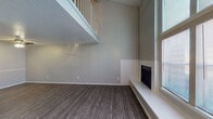 This two-story residence offers a thoughtfully designed layout across two levels, combining practical functionality with comfortable living. The entry welcomes you through a classic six-panel front door with wood-look flooring that extends throughout the main level. The living room is an immediate standout, featuring dramatic vaulted ceilings that soar to the upper floor, where a white-railed balcony overlooks the space below. Natural light streams in through large windows, while a fireplace with a tiled hearth adds a warm focal point to the room. The kitchen is outfitted with bold dark cabinetry, light stone-look countertops, a peninsula for additional prep space, and black appliances, all set atop wood-look flooring. A dedicated dining or flex room on the main level features a ceiling fan and additional closet space. A staircase with a handrail leads to the upper level, where carpeted bedrooms provide a comfortable retreat. The primary bedroom connects directly to a private bathroom featuring dark vanity cabinetry, a stone-look countertop, and a well-lit mirror. A full bathroom with a tiled tub-shower combination and wood-look flooring serves the remaining rooms. The upper level also includes an open loft-style space with carpet flooring, bathed in neutral tones throughout.