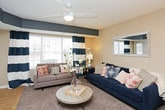 This single-floor residence offers a thoughtfully organized layout that balances open communal spaces with private retreats. The living room serves as the heart of the home, featuring plush carpet, a ceiling fan, and large windows with exterior access that flood the space with natural light and provide outdoor views. Bold accent walls in deep teal add a distinct visual character to the living area.

The kitchen is well-equipped with rich wood cabinetry, stainless steel appliances including a refrigerator, range, and over-the-range microwave, and light-toned countertops. A peninsula with bar seating bridges the kitchen and the adjacent space, making it ideal for casual dining or entertaining. Light hardwood-style flooring runs throughout the kitchen area.

The bedrooms are carpeted and neutral in tone, offering a calm and restful atmosphere. The primary bedroom is generously proportioned with windows and direct access to the living area. A second bedroom provides a comfortable, versatile space with its own window and closet access.

The bathroom includes a full tub-shower combination with tile flooring and a vanity with wood cabinetry. A dedicated laundry room houses a full-size washer and dryer with overhead wire shelving for added storage.