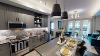 Located in the heart of downtown Phoenix, this single-floor residence at 125 E Washington St combines contemporary design with thoughtful functionality. The open-concept kitchen is a standout feature, showcasing charcoal-toned shaker cabinetry, dark quartz countertops, a mosaic tile backseat with under-cabinet lighting, a farmhouse sink, and a full suite of stainless steel appliances including a gas range and side-by-side refrigerator. A central island with seating provides additional prep and dining space, illuminated by bold black pendant lights overhead.

The living area flows naturally from the kitchen and is anchored by tray ceilings, a gold-toned chandelier, and French doors opening onto a private balcony with urban views. The space carries a rich, jewel-toned aesthetic throughout.

Both bedrooms offer carpet flooring, large windows with city views, and generous closet space, including a walk-in closet with adjustable shelving. The primary bathroom features a double-sink vanity with dark countertops, white cabinetry, large-format tile flooring, and a glass-enclosed walk-in shower. Dark hardwood-style flooring throughout the main living areas ties the sophisticated color palette together, creating a cohesive and polished urban retreat.