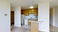 This single-floor space offers a practical and well-organized layout designed for everyday comfort. The kitchen is a standout feature, showcasing warm oak cabinetry that spans both upper and lower sections, providing ample storage for all essentials. White appliances, including a refrigerator and dishwasher, are neatly integrated into the space, while a stainless steel sink sits beneath additional cabinetry. A peninsula-style breakfast bar extends from the kitchen, offering a convenient surface for casual dining or meal prep while maintaining an open connection to the adjoining living area. The kitchen is finished with light tile flooring, which transitions to carpet in the surrounding living spaces, creating a clear and functional distinction between areas. Flush-mount ceiling lighting keeps the kitchen well-illuminated. The overall design is clean and straightforward, with neutral wall tones throughout that contribute to a bright and open atmosphere. The layout makes efficient use of the available space, ensuring that each area serves a clear purpose while maintaining a cohesive and livable environment.