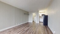 Located at 3129 Sinton Rd in Colorado Springs, Colorado, this single-floor studio unit offers a practical and efficiently designed layout ideal for comfortable everyday living. The main living area is open and versatile, finished with durable wood-look plank flooring that runs throughout the space, complemented by neutral gray walls and a textured ceiling. A wall-mounted clothing rack provides convenient built-in storage within the living area. Large vertical-blind-covered windows along the front of the unit allow ample natural light to fill the room, creating a bright and airy atmosphere. The compact kitchenette is neatly appointed with crisp white cabinetry, stone-patterned granite-style countertops, a stainless steel single-basin sink, a cooktop, an over-the-range stainless steel microwave, and a full-size refrigerator — offering all essential cooking amenities in a well-organized space. The bathroom features classic white subway tile wainscoting, wood-look flooring, a white vanity with storage, a wall-mounted mirror, a window for natural ventilation, and a full tub and shower combination. The unit's clean, move-in-ready condition and functional design make it a straightforward and practical living space in Colorado Springs.
