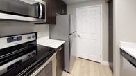 This single-floor residential unit offers a thoughtfully designed layout with a cohesive neutral color palette and a blend of durable hard-surface and soft flooring throughout. The open living and dining area features smooth hardwood-style flooring, a ceiling fan with integrated lighting, and multiple windows dressed with slatted blinds that invite abundant natural light. A glass-paneled exterior door provides direct outdoor access, enhancing the sense of connectivity to the outside. The kitchen is outfitted with dark espresso cabinetry, white countertops, and a full suite of stainless steel appliances including a refrigerator, electric range, microwave, and dishwasher, all set on light hardwood-style flooring. The bedrooms are generously sized, finished with plush neutral carpeting and large windows that frame outdoor views and flood the rooms with natural light. The two bathrooms are clean and functional: one features a dark-cabinet vanity with a white countertop, a framed mirror, brushed nickel fixtures, and a window for ventilation, while the second includes a soaking tub with shower combination and tile surround. Throughout the unit, white trim, neutral taupe walls, and consistent finishes create a modern, move-in-ready atmosphere.