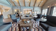 Located at 1235 Ashley Gardens Blvd in Charleston, SC, this single-story community clubhouse is a beautifully designed gathering space that blends coastal charm with modern elegance. The centerpiece of the facility is a grand open living area crowned by soaring vaulted ceilings with exposed wood beams and tongue-and-groove pine, bathed in natural light from large windows and French doors that offer views of the outdoor pool area. Multiple seating arrangements—featuring wingback chairs, plush sofas, and patterned area rugs—create versatile spaces for both relaxation and socializing. The fully equipped kitchen is a standout, showcasing bold teal cabinetry paired with crisp white uppers, a striking herringbone tile backsplash, a generous island with white quartz countertops, stainless steel appliances, and woven pendant lights overhead. A dedicated game area accommodates a full-size pool table beneath warm pendant lighting and floor-to-ceiling windows. A charming built-in coffee and beverage bar, complete with a coffee machine and a glass-front mini refrigerator, adds convenience. Smaller seating nooks near the entry provide intimate spaces for quiet conversation. Wide-plank hardwood flooring flows throughout, tying together the space's coastal, transitional aesthetic.