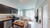 Located at 7065 Banyan Leaf Drive in West Palm Beach, Florida, this single-floor residence offers a well-designed, contemporary interior with a cohesive neutral palette and modern finishes throughout. The open-concept layout seamlessly connects the kitchen, dining, and living areas, creating a spacious and functional flow.

The kitchen is outfitted with dark cabinetry featuring under-cabinet lighting, granite countertops, a tile backsplash, and a full suite of stainless steel appliances. A dining area adjacent to the kitchen comfortably accommodates a full table and chairs, making it an ideal space for entertaining.

The living room is bright and airy, benefiting from large sliding glass doors that invite abundant natural light and provide direct views of the surrounding greenery. A built-in wooden media wall adds warmth and texture to the space. Light wood-style flooring runs throughout the main living areas.

The bedrooms are calm and well-proportioned. The primary bedroom features floor-to-ceiling mirrored closet panels that enhance the sense of space. A secondary bedroom is bright and versatile. Both bathrooms are finished with granite-topped vanities, dark cabinetry, and tile flooring, offering clean, modern aesthetics.