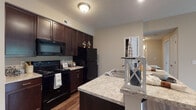 Located at 700 Reynoldsburg New Albany Rd in Blacklick, Ohio, this single-floor residence offers a thoughtfully designed layout with a cohesive, neutral color palette throughout. The kitchen is a standout feature, showcasing rich dark espresso cabinetry paired with light granite-style countertops that extend to a peninsula with a built-in sink — ideal for both meal prep and casual dining. Black appliances, including a refrigerator, electric range, and over-the-range microwave, complement the cabinetry for a unified aesthetic. Warm wood-look flooring runs throughout the kitchen and living areas, adding depth and continuity to the space. A dedicated pantry closet off the kitchen provides convenient additional storage. The open layout connects the kitchen to a bright living area that benefits from natural light through a sliding glass door. The bedroom is carpeted for comfort and features a sliding closet door with built-in shelving. The full bathroom is well-appointed with a tub-shower combination, a vanity with a granite-style countertop, dark cabinetry, tile flooring, and a large mirror. Neutral wall tones and clean finishes throughout create a warm, move-in-ready atmosphere well-suited for everyday living.