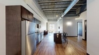 Located in the heart of downtown Syracuse at 324 W Water Street, this two-bedroom, two-bathroom unit blends industrial loft character with modern finishes across a single, well-organized floor. The living room makes a strong first impression with soaring ceilings, exposed ductwork, and light-toned hardwood flooring that runs throughout the main living areas. A large window allows natural light to fill the space while offering views of the surrounding cityscape, creating an open and airy atmosphere. The kitchen is outfitted with rich dark-stained cabinetry, dark granite countertops, and a full suite of stainless steel appliances including a refrigerator, range, microwave, and dishwasher. Both bedrooms feature exposed light brick accent walls that lend warmth and texture to the rooms, complemented by hardwood-style flooring and dark-framed doors. The spacious primary bedroom provides a generous layout with ample room to furnish comfortably. The two bathrooms are finished with large-format light tile flooring, dark vanity cabinetry with granite countertops, and clean white fixtures. A hallway connects the rooms efficiently, and the overall layout offers a practical flow throughout the unit. This space delivers an urban industrial aesthetic with quality modern finishes throughout.