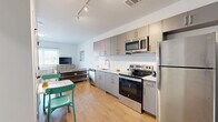Unit 602 at 1 East Main Street in Bound Brook, NJ offers a thoughtfully designed one-bedroom, one-bathroom residence with a contemporary aesthetic and efficient use of space. The open-plan living area seamlessly integrates the kitchen, dining, and living zones, creating a bright and cohesive environment bathed in natural light from large windows. Light hardwood flooring flows throughout the unit, enhancing the airy feel.

The kitchen is well-appointed with sleek grey flat-front cabinetry, a distinctive white hexagonal tile backsplash, and a full suite of stainless steel appliances including a refrigerator, electric range, microwave, and dishwasher. A dining area adjacent to the kitchen provides a functional space for everyday meals. The living area offers a comfortable retreat with access to a large window overlooking the surroundings.

The bedroom is a calm, light-filled space featuring a wide window with horizontal blinds and ample room for a full furniture arrangement. A dedicated closet provides practical storage. The bathroom is finished in a clean, minimalist style with white tile flooring, a grey vanity with a stone-topped sink, a mirror, and chrome fixtures. Track lighting throughout the main living area adds a modern design touch, rounding out this well-appointed urban residence.