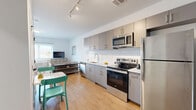 Unit 602 at 1 East Main Street in Bound Brook, NJ offers a thoughtfully designed one-bedroom, one-bathroom residence with a contemporary aesthetic and efficient use of space. The open-plan living area seamlessly integrates the kitchen, dining, and living zones, creating a bright and cohesive environment bathed in natural light from large windows. Light hardwood flooring flows throughout the unit, enhancing the airy feel.

The kitchen is well-appointed with sleek grey flat-front cabinetry, a distinctive white hexagonal tile backsplash, and a full suite of stainless steel appliances including a refrigerator, electric range, microwave, and dishwasher. A dining area adjacent to the kitchen provides a functional space for everyday meals. The living area offers a comfortable retreat with access to a large window overlooking the surroundings.

The bedroom is a calm, light-filled space featuring a wide window with horizontal blinds and ample room for a full furniture arrangement. A dedicated closet provides practical storage. The bathroom is finished in a clean, minimalist style with white tile flooring, a grey vanity with a stone-topped sink, a mirror, and chrome fixtures. Track lighting throughout the main living area adds a modern design touch, rounding out this well-appointed urban residence.