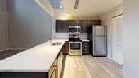 Located at 1117 Euclid Ave in Cleveland, OH, this multi-level residence spans three floors and combines contemporary design with functional living spaces. The layout is connected by a staircase rising through a dramatic double-height volume, with light wood-style flooring on the main level transitioning to plush carpeting in the upper rooms.

The kitchen is outfitted with dark espresso cabinetry, stainless steel appliances including a range, microwave, and refrigerator, and an extended white countertop with an undermount sink. A geometric tile backsplash adds visual interest against the neutral palette.

Bathrooms feature wood-look tile flooring, dark vanity cabinetry with quartz-style countertops, undermount sinks, brushed nickel fixtures, and tiled tub-shower combinations with large-format tile surrounds. Grab bars are present, reflecting accessible design considerations.

Bedrooms are carpeted and neutral-toned, with one featuring a private en-suite bathroom. A spacious walk-in closet with wire shelving and hanging rods provides generous storage. An interior window connects one room to the multi-story atrium, while large exterior windows on upper levels offer views of the Cleveland skyline, bringing natural light deep into the space.