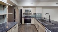 This 950-square-foot, single-story residence at 7909 Venture Center Way in Boynton Beach, Florida offers a well-designed layout across 2 bedrooms, 1 bathroom, and 4 closets, with an in-unit laundry area. The open-concept kitchen and living room serve as the heart of the home, featuring striking dark granite countertops, white shaker cabinetry, a teal subway tile backsplash, stainless steel appliances, and durable hardwood-style flooring. A peninsula with a built-in sink adds both functionality and visual appeal. The living area extends to a private patio through sliding glass doors, allowing natural light and outdoor views of lush greenery. Both bedrooms are carpeted and equipped with ceiling fans; the 240-square-foot primary bedroom includes closet access and windows framing serene outdoor scenery. The second bedroom also benefits from natural light and a ceiling fan. The shared full bathroom is finished with white subway tile, a tub-shower combination, dual vanity with granite countertops, light wood cabinetry, and classic white tile flooring. With four closets distributed throughout the unit, storage is plentiful. The clean, neutral palette and modern finishes create a cohesive and functional living environment.