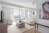 Located in Oakville's sought-after Bronte neighbourhood, this modern 2-bedroom, 1-bathroom residence offers a bright, open-concept layout finished in a clean, neutral palette throughout. The spacious living and dining area is anchored by large floor-to-ceiling windows that frame sweeping views of Lake Ontario and the surrounding Bronte waterfront, flooding the space with natural light and creating an airy, sophisticated ambiance. Light hardwood-style flooring runs throughout the main living areas, complementing the contemporary design.

The kitchen is thoughtfully designed with sleek two-tone cabinetry, quartz-style countertops, a glass tile backsplash, and a full suite of stainless steel appliances, including a built-in dishwasher and over-the-range microwave. An extended peninsula provides additional prep and dining space.

The generously sized primary bedroom features a large window with a roller shade and ample closet space with sliding panel doors. The second bedroom, versatile in use, also enjoys natural light and urban views. The full bathroom is finished with clean white subway tile, a soaker tub with overhead shower, and warm wood-tone cabinetry with a stone-finish countertop. A dedicated closet provides additional storage, completing this well-appointed residence.
