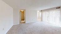 This single-floor residence offers a straightforward and functional layout, as visible in the overhead floor plan view. The living area is generously sized, finished with neutral-toned wall-to-wall carpeting and crisp white walls that create a clean, bright atmosphere. A hallway connects the main living space to the rest of the unit, with a sliding glass door allowing natural light to filter into the living area.

The kitchen is equipped with warm oak cabinetry offering ample storage above and below the countertops. White laminate counters and a white electric range with a built-in overhead ventilation hood complete the functional cooking space. A peninsula-style counter is visible in the floor plan, suggesting an open connection to the adjacent living area.

The bedrooms are carpeted and well-proportioned, each featuring white walls and dedicated closet space. One bedroom includes a walk-in closet, while others feature reach-in closets with rod storage. Windows fitted with horizontal blinds provide natural light.

The bathroom includes light-blue tiled walls surrounding a full-size soaking tub with an overhead shower, a toilet, and light tile flooring, maintaining the home's clean, neutral aesthetic throughout.
