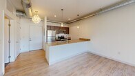 Located at 601 Lake Michigan Drive in Grand Rapids, Michigan, this one-bedroom, one-bathroom unit offers a well-designed, efficient layout with a contemporary industrial aesthetic. The open-concept living and kitchen area anchors the space, featuring light hardwood-style flooring, exposed ductwork along the ceiling, and pendant lighting that adds a modern urban character. The kitchen is thoughtfully appointed with dark espresso cabinetry, granite countertops, stainless steel appliances including a refrigerator, range, and microwave, and a peninsula with an undermount sink — ideal for both cooking and casual dining. Recessed lighting and pendant fixtures illuminate the space warmly. The bedroom offers a comfortable, carpeted retreat with a closet, exposed ductwork that reinforces the industrial design theme, and access to natural light through a window. The full bathroom is finished with large-format tile flooring, a granite-topped vanity with warm wood cabinetry, a full soaking tub and shower combo, and clean white walls. Throughout the unit, crisp white walls and consistent finishes create a cohesive, move-in-ready environment suited for urban living in the heart of Grand Rapids.