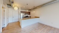 Located at 601 Lake Michigan Drive in Grand Rapids, Michigan, this one-bedroom, one-bathroom unit offers a well-designed, efficient layout with a contemporary industrial aesthetic. The open-concept living and kitchen area anchors the space, featuring light hardwood-style flooring, exposed ductwork along the ceiling, and pendant lighting that adds a modern urban character. The kitchen is thoughtfully appointed with dark espresso cabinetry, granite countertops, stainless steel appliances including a refrigerator, range, and microwave, and a peninsula with an undermount sink — ideal for both cooking and casual dining. Recessed lighting and pendant fixtures illuminate the space warmly. The bedroom offers a comfortable, carpeted retreat with a closet, exposed ductwork that reinforces the industrial design theme, and access to natural light through a window. The full bathroom is finished with large-format tile flooring, a granite-topped vanity with warm wood cabinetry, a full soaking tub and shower combo, and clean white walls. Throughout the unit, crisp white walls and consistent finishes create a cohesive, move-in-ready environment suited for urban living in the heart of Grand Rapids.