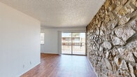 Located at 1301 Avalon Dr in El Paso, TX, this one-bedroom, one-bathroom unit offers a well-organized single-floor layout designed for comfortable everyday living. The combined kitchen and living area serves as the heart of the home, immediately drawing attention with a dramatic full-height stacked-stone accent wall that adds texture and character throughout. Wood-look flooring runs across the living space and kitchen, contributing warmth and visual continuity. A sliding glass door opens to a private balcony, flooding the room with natural light and offering open outdoor views. The kitchen is efficiently arranged with white cabinetry, light stone-look countertops, and matching white appliances including a refrigerator and electric range. The bedroom continues the stacked-stone accent wall motif, complemented by soft carpeting, a ceiling fan, and a wide window that brings in additional natural light. A generously sized double sliding-door closet provides ample storage. The bathroom features a full tub and shower combo enclosed by clean, neutral large-format tile. Textured ceilings are consistent throughout the unit, adding a classic touch to the overall aesthetic. This unit offers a distinctive design character within a compact and functional footprint.