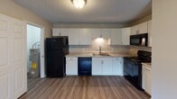 Located at 1816 McKnight Mill Rd in Greensboro, NC, this single-story unit offers a practical and well-organized layout designed for comfortable everyday living. The entry foyer features wood-look vinyl flooring and a painted brick accent wall, providing a welcoming introduction to the space.

The kitchen is a functional highlight, outfitted with white shaker-style cabinetry, light granite-look countertops, and a full suite of black appliances including a refrigerator, electric range, over-the-range microwave, and dishwasher. Wood-look vinyl flooring extends throughout the kitchen, complementing the clean, neutral color palette.

The living and bedroom areas are finished with patterned carpet and neutral wall tones, with some rooms showcasing painted brick accent walls that add architectural character. Bedrooms receive natural light through blinds-fitted windows, creating a bright and airy feel.

Two bathrooms serve the unit: one featuring a combined tub and shower with a curved curtain rod and wood-look flooring, and a second with a white vanity, framed mirror, and vanity lighting. A dedicated utility area houses a water heater and washer/dryer hookups, offering added convenience for in-unit laundry setup.