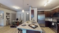 Located at 3500 Carrington Mill Blvd in Morrisville, NC, this single-floor residence combines contemporary design with functional living spaces throughout. The open-concept kitchen serves as a central hub, showcasing granite countertops, rich dark wood cabinetry, stainless steel appliances including a large side-by-side refrigerator, and a built-in wine rack overhead. A granite-topped kitchen island with pendant lighting above provides additional prep space and casual seating, while an adjacent dining area completes the entertaining zone.

The living room features striking dark accent walls, wood-look flooring, crown molding, and natural light from multiple windows dressed with patterned curtains. Ceiling fans are present throughout the residence. Multiple bedrooms offer plush carpeting, natural light, and ample closet space, including a walk-in closet with built-in shelving. The bathroom is finished with wood-look tile flooring, a glass-enclosed shower with subway tile surround, a dark wood vanity with stone countertops, and access to the walk-in closet. Each room reflects a cohesive, modern aesthetic with careful attention to finish quality and detail.