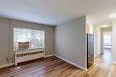 Located at 7301–7317 Riggs Rd in Hyattsville, MD, this 1-bedroom, 1-bathroom unit offers a thoughtfully organized single-floor layout. The living room greets you at the entrance with warm hardwood-style flooring, neutral gray walls, and a flush-mount ceiling light, creating a bright and welcoming atmosphere. A hallway connects the main living areas, providing a smooth flow throughout the unit. The kitchen is positioned off the living area and features stainless steel appliances, including a refrigerator. The bedroom offers a comfortable, private retreat with its own window that allows natural light and outdoor greenery views, a baseboard radiator for heating, a window-mounted air conditioning unit, and a built-in closet with bifold doors. Two additional closets throughout the unit provide generous storage. The bathroom is finished with full-height ceramic tile surrounding the soaking tub and shower combo, complemented by a small window for natural ventilation. Hardwood-style flooring runs consistently through the living and bedroom areas, tying the space together with a cohesive, clean aesthetic. The unit includes three closets in total, ensuring ample storage for everyday living.