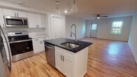 This well-appointed 2-bedroom, 2-bathroom single-floor residence combines modern finishes with a thoughtful, open layout. The heart of the home is a contemporary kitchen featuring a central island with a dark granite countertop, undermount stainless steel sink, and decorative geometric pendant lighting. White shaker-style cabinetry lines the walls, complemented by light quartz countertops and a full suite of stainless steel appliances, including a range, over-the-range microwave, dishwasher, and refrigerator. Warm hardwood flooring flows seamlessly from the kitchen into the open living area, which is illuminated by recessed lighting and a ceiling fan. The bedrooms offer a clean, bright atmosphere with large windows that invite natural light and views of surrounding greenery, accented by modern light fixtures and the same rich hardwood floors. The primary bathroom is elegantly finished with marble-style tile covering both the floors and tub surround, a dark wood vanity, and a soaking tub. The second bathroom features clean white subway tile in the tub and shower area with neutral floor tile. A spacious walk-in closet with built-in shelving and multiple hanging rods provides generous storage. The overall aesthetic is fresh, modern, and move-in ready.