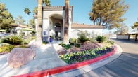 This inviting outdoor community space is defined by its resort-style design and Mediterranean-influenced architecture, characterized by stucco exteriors, terracotta tile rooflines, and graceful arched entryways. At the heart of the space is a generously sized swimming pool with vivid turquoise water, complemented by a decorative stone water feature that adds both visual interest and a soothing ambiance. Adjacent to the pool, a dedicated spa offers a relaxing retreat with active water jets.

The surrounding sun deck is thoughtfully furnished with cushioned chaise lounges and multiple lime-green patio umbrellas, providing ample shade for outdoor relaxation. A dedicated outdoor kitchen area features dual stainless steel built-in gas grills mounted on a stone-finished counter, making it well-suited for communal gatherings and outdoor dining.

Seating areas scattered throughout the courtyard are outfitted with colorful chairs and tables shaded by additional umbrellas, creating a lively and welcoming atmosphere. Tall palm trees and mature shade trees frame the entire outdoor area, enhancing privacy and adding to the desert resort aesthetic. The main entrance is highlighted by manicured desert landscaping, including decorative boulders and vibrant seasonal flowers, contributing to a polished and well-maintained first impression.