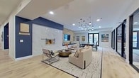 Located at 870 S SH 161 Frontage Rd in Grand Prairie, Texas, this single-floor community amenity space offers a generously sized, open-concept layout designed with contemporary sophistication. The main gathering area serves as the centerpiece of the space, anchored by a striking floor-to-ceiling marble-clad fireplace flanked by geometric wood accent panels and a built-in bench. Stylish pendant lighting — including a dramatic cluster chandelier — illuminates the seating and dining areas, which flow seamlessly across light-toned hardwood flooring. The fully equipped kitchen features a large marble-topped island with bar seating, a combination of dark and white cabinetry, a textured tile backsplash, stainless steel appliances, and globe pendant lights with brass accents. A dedicated lounge zone offers additional seating and a wall-mounted flat-screen TV, ideal for casual gatherings. Glass-partitioned private rooms, visible from the main floor, provide quieter settings suitable for meetings or focused work. Deep navy blue accent walls contrast elegantly with the bright white ceilings and natural light streaming in through large glass doors and windows, creating a polished, inviting atmosphere throughout.