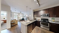 Located at 8011 Augusta Pines Dr in Spring, TX, this one-bedroom, one-bathroom residence offers a thoughtfully designed open-concept layout. The living area features warm hardwood-style flooring, a ceiling fan, and a seamless flow into the kitchen, creating an inviting and functional space. The kitchen is a standout feature, equipped with rich dark cabinetry, granite-style countertops, a peninsula with bar seating, pendant lighting, track lighting, and a full suite of stainless steel appliances including a refrigerator, range, microwave, and dishwasher. The open sightlines from the kitchen to the living room enhance the sense of spaciousness throughout. The generously sized primary bedroom is carpeted for comfort and includes a ceiling fan, natural light from a large window with blinds, and access to a dedicated walk-in closet with built-in wire shelving. The bathroom offers dark cabinetry with a granite-topped vanity, hardwood-style flooring, and a full soaking tub with tile surround. Throughout the residence, neutral tones and clean finishes contribute to a modern, cohesive aesthetic that is both practical and comfortable.
