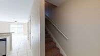 This two-story home is thoughtfully laid out across two levels connected by a carpeted staircase fitted with a white handrail. The lower level features an open-concept kitchen finished with white cabinetry, light-toned countertops, a mosaic tile backsplash, and stainless steel appliances including a range, microwave, and dishwasher. Large white floor tiles extend throughout the lower level, contributing to a bright, clean aesthetic. A ceiling fan with a pendant light fixture overhead adds both function and visual interest to the kitchen and adjoining living area. Natural light filters in through windows dressed with vertical blinds. The upper level hosts carpeted bedrooms, each equipped with ceiling fans and windows that allow natural light to brighten the rooms. The neutral-toned walls and plush carpeting create a comfortable, relaxed atmosphere throughout. The bathrooms are finished with white tile, featuring a tub-shower combination, granite-style countertops, and tile flooring. Overall, the home maintains a consistent neutral palette, providing a versatile and move-in ready environment across both floors.