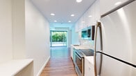 Located at 1335 Boylston St, Unit 507 in Boston's vibrant Fenway neighborhood, this modern one-bedroom, one-bathroom residence offers a thoughtfully designed layout across a single floor. The unit is entered through a welcoming entrance corridor that flows naturally into the open kitchen and living areas.

The galley-style kitchen is outfitted with high-gloss white cabinetry, white subway tile backsplash, light stone countertops, and a full suite of stainless steel appliances, including a range, built-in microwave, and refrigerator. Recessed lighting illuminates the clean, contemporary finishes throughout.

Warm hardwood flooring runs continuously through the main living areas and into the bedroom, creating a cohesive and inviting atmosphere. The living area is anchored by expansive floor-to-ceiling sliding glass windows that frame lush greenery outside, flooding the space with natural light and providing a tranquil, nature-facing outlook.

The bedroom is a well-proportioned retreat featuring a closet with double doors, clean white walls, and direct access to the same verdant outdoor view through large-format windows. The bathroom is finished with terracotta tile flooring, crisp white walls, and a glass-enclosed shower stall, offering a functional and clean aesthetic.