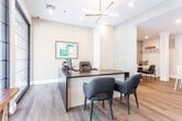 Located at 38 Old Short Hills Rd in Livingston, NJ, this thoughtfully designed single-floor commercial space combines functionality with modern aesthetics throughout. Warm hardwood flooring flows seamlessly across the entire layout, creating a cohesive and inviting atmosphere.

The front office area is a standout feature, boasting a full wall of floor-to-ceiling glass panels that flood the room with natural light and offer clear views to the exterior. A sleek, dark executive desk with guest seating, recessed lighting, and a contemporary linear pendant fixture complete this professional setting. Textured accent wall paneling adds a refined touch to the space.

The kitchen is well-appointed with light shaker-style cabinetry, crisp white quartz countertops, a classic subway tile backsplash, and stainless steel appliances including a refrigerator and over-the-range microwave. A central island with bar seating serves as a practical and social hub, illuminated by pendant lighting overhead.

Adjacent to the kitchen, a charming breakroom nook features built-in bench seating with a textured accent wall, a round marble-top pedestal table, and a dedicated mudroom-style storage wall with hooks and shelving — perfect for a comfortable and organized shared workspace environment.