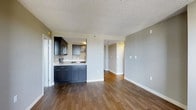 Located at 401 Cumberland in South Portland, Maine, this single-floor residence offers a clean, modern aesthetic with a thoughtfully designed open-concept layout. Rich, dark hardwood flooring flows seamlessly throughout the main living areas, providing a warm contrast to the light gray walls and bright white trim that define the interior palette. The textured ceiling adds subtle character to the space. The kitchen is positioned in an open, accessible configuration and features dark navy cabinetry with sleek hardware, light countertops, and stainless steel appliances, including a microwave and range. The kitchen transitions naturally into the open living area, creating an inviting, connected space well-suited for both everyday living and entertaining. A hallway leads further into the unit, suggesting additional private living spaces beyond the main area. Natural light enters the space, enhancing the airy, clean feel of the interior. The overall ambiance is contemporary and functional, with a neutral color scheme that offers versatility in furnishing and décor. This residence presents a polished, move-in-ready environment in a convenient South Portland location.