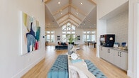 Located in Tampa, FL, this single-story community clubhouse offers a thoughtfully designed, multi-functional layout spanning a generous footprint. The centerpiece is a soaring great room with dramatic vaulted ceilings accented by exposed wood beams, recessed lighting, and light hardwood flooring. Floor-to-ceiling windows flood the space with natural light and provide open views of the surrounding landscape, creating a bright and welcoming atmosphere. Comfortable lounge seating, vibrant artwork, and a billiards table contribute to the social, resort-style ambiance.

Adjacent dining areas feature large communal tables beneath striking pendant light fixtures, complemented by a wet bar with a pearlescent tile backsplash — ideal for gatherings and events. Smaller breakout dining rooms offer more intimate settings, complete with glass-top tables, teal velvet seating, and decorative lighting.

Private meeting rooms are enclosed by glass French doors, offering natural light, patterned carpeting, and a clean, professional aesthetic suitable for focused work or small group collaboration. Cozy lounge nooks with built-in bench seating and decorative mirrors provide additional transitional spaces throughout the hallways.

The dedicated fitness center is generously sized and well-appointed with cardio machines, free weights, a squat rack, and large windows that bring in ample daylight, all set on patterned tile flooring with ceiling fans overhead.