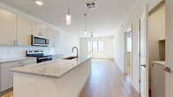 This well-designed one-bedroom, one-bathroom unit offers a thoughtfully organized single-floor layout. The open-concept kitchen and living area forms the heart of the unit, anchored by a large granite-topped island with an undermount sink and pendant lighting overhead. The kitchen is fully equipped with stainless steel appliances, including a French door refrigerator, electric range, and built-in microwave, complemented by flat-front cabinetry in a soft neutral tone and a white subway tile backsplash. Light hardwood flooring extends throughout the main living areas, contributing to a clean, contemporary aesthetic. A ceiling fan and large windows in the living area allow for natural light and outdoor views.

The bedroom is carpeted for comfort and features a dedicated window with outdoor views, providing a calm, naturally lit retreat. An additional room with hardwood flooring and a glazed exterior door offers versatile use as a secondary living or flex space. The bathroom includes a granite-topped vanity with under-cabinet storage, and directly adjoins a walk-in closet with built-in shelving. Neutral wall tones and consistent finishes throughout create a cohesive, modern ambiance across the entire unit.