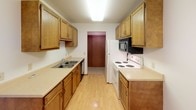 Located at 2900 S Louise Ave in Sioux Falls, South Dakota, this single-floor unit offers a straightforward, functional layout well-suited for everyday living. The galley-style kitchen is efficiently designed, featuring warm oak cabinetry lining both walls, light laminate countertops, a double-basin sink, a white electric range with overhead microwave, a full-size refrigerator, and a dishwasher. Light wood-tone flooring runs throughout the kitchen, adding a clean, bright feel to the space.

The living area is carpeted and open, with a wall-mounted air conditioning unit and a sliding door or window providing natural light and outdoor views. A ceiling fan with integrated lighting is present in the adjacent room, which also features neutral carpet, a window overlooking greenery, and a baseboard heating system. The layout, as seen in the floor plan, includes a defined bedroom, bathroom, and living space with clear circulation between areas.

The bathroom is finished with tile flooring, a single-sink vanity with oak cabinetry, a wall-mounted medicine cabinet, and a full tub-shower combination. Textured ceilings are consistent throughout the unit, contributing to a classic residential character. Overall, the space presents a clean, practical interior with functional amenities.