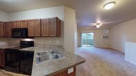 Located at 4569 Driver Lane in Coeur d'Alene, Idaho, this two-floor unit offers a practical and comfortable layout designed for everyday living. The kitchen is well-appointed with rich wood cabinetry, laminate countertops, a double-basin sink, and black Whirlpool appliances including an electric range, over-the-range microwave, and dishwasher. Wood-style flooring grounds the kitchen space, which opens to a carpeted living area featuring a ceiling fan and a sliding glass door leading to a private balcony with views of surrounding greenery. Soft, neutral carpeting flows throughout the living and bedroom areas, creating a warm and cohesive feel. The bedrooms are generously sized with large windows that invite natural light and offer views of the outdoors. The bathroom features a soaking tub with tiled surround and chrome fixtures. A dedicated in-unit laundry area accommodates a full-size washer and dryer, with shelving above for added storage. The attached single-car garage includes an automatic door opener and houses the water heater and HVAC system, providing convenient and practical utility access. The overall color palette is neutral and understated, lending the space a clean, move-in-ready character throughout.