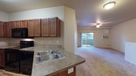 Located at 4569 Driver Lane in Coeur d'Alene, Idaho, this two-floor unit offers a practical and comfortable layout designed for everyday living. The kitchen is well-appointed with rich wood cabinetry, laminate countertops, a double-basin sink, and black Whirlpool appliances including an electric range, over-the-range microwave, and dishwasher. Wood-style flooring grounds the kitchen space, which opens to a carpeted living area featuring a ceiling fan and a sliding glass door leading to a private balcony with views of surrounding greenery. Soft, neutral carpeting flows throughout the living and bedroom areas, creating a warm and cohesive feel. The bedrooms are generously sized with large windows that invite natural light and offer views of the outdoors. The bathroom features a soaking tub with tiled surround and chrome fixtures. A dedicated in-unit laundry area accommodates a full-size washer and dryer, with shelving above for added storage. The attached single-car garage includes an automatic door opener and houses the water heater and HVAC system, providing convenient and practical utility access. The overall color palette is neutral and understated, lending the space a clean, move-in-ready character throughout.