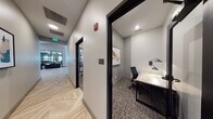 Located at 14750 S Wallin Dr in Plainfield, IL, this single-floor professional workspace combines contemporary design with practical functionality. The layout is anchored by a well-appointed conference room enclosed by striking black-framed glass partition walls, offering visibility into the broader space while maintaining a sense of privacy. Inside, a sleek oval dark conference table is surrounded by light wood chairs, and a large wall-mounted display screen serves as a focal point for presentations and collaboration. Pendant track lighting adds a modern, refined touch overhead.

A series of private study nooks line the corridors, each outfitted with a light wood built-in desk, an ergonomic mesh chair, and dual adjustable wall-mounted task lamps that provide focused illumination. Framed abstract artwork adorns the walls of each nook, adding a thoughtful aesthetic touch to these compact, distraction-free work areas.

The hallways connecting these spaces are a design highlight in their own right, featuring a bold chevron-patterned hardwood floor that adds visual depth and sophistication. Neutral gray walls and black door trim create a clean, polished contrast throughout. At the end of the corridor, an open lounge area with modern furnishings and large windows is visible, hinting at a welcoming communal zone that completes this well-designed, professional environment.