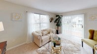 This single-floor residence offers a thoughtfully designed layout with a cohesive, neutral aesthetic throughout. The living area is bright and welcoming, featuring plush carpeting, large windows dressed with sheer white curtains, and sliding glass doors that open to an outdoor space, filling the room with natural light and exterior views. An adjacent sitting or flex area provides additional functional space, also carpeted and naturally lit.

The galley-style kitchen is efficiently arranged with white cabinetry, granite-style countertops, dark hardwood-style flooring, and stainless steel appliances including a refrigerator, range, and built-in microwave. A dedicated dining area sits nearby, featuring dark hardwood-style flooring, a ceiling fan, and a window overlooking the surroundings.

The primary bedroom includes plush carpeting, a walk-in closet, and access to an en-suite bathroom. The en-suite features a granite vanity, tile flooring, and a shower-tub combination. Additional bedrooms are carpeted and well-sized, each with natural light. A second full bathroom mirrors the finishes of the primary, with a granite-top vanity and tile floors. Textured ceilings are consistent throughout, adding a classic residential character to the space.