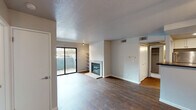 This single-floor unit at 4005 Crowell Blvd in Davis, California offers a well-designed, functional layout with a clean, neutral aesthetic throughout. The open-concept living and dining area serves as the heart of the home, featuring rich dark hardwood-style flooring, a textured ceiling, and a classic brick fireplace with a glass screen that adds warmth and character. Built-in shelving flanks the fireplace, providing convenient display and storage space. Sliding glass doors lead directly to a private balcony, allowing natural light to fill the living space and offering a view of the surrounding greenery. The kitchen is positioned adjacent to the living area with a raised breakfast bar peninsula, white cabinetry, dark countertops, recessed lighting, and stainless steel appliances including a refrigerator, microwave, and electric range. A hallway connects the living area to the private spaces of the unit, including carpeted bedrooms with windows that bring in natural light. The bathroom features white cabinetry, a dark countertop vanity, and a combined tub and shower. Throughout the unit, a consistent palette of white walls, dark flooring, and clean finishes contributes to a cohesive, move-in ready atmosphere.
