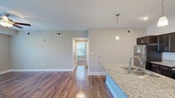 Located at 19 E Revere Blvd in Huntsville, Alabama, this single-floor, one-bedroom, one-bathroom residence offers a thoughtfully designed open-concept layout. The living room is a welcoming space featuring rich hardwood-style flooring, a ceiling fan with light fixture, and glass French doors that invite natural light and provide outdoor access. The kitchen is a standout highlight, showcasing dark espresso cabinetry, a white subway tile backsplash, stainless steel appliances including a refrigerator, range, and microwave, and a generous granite-topped island with an undermount sink illuminated by pendant lighting. The hallway connects the main living areas and includes tile flooring, access to a utility closet, and an electrical panel. The spacious bedroom is finished with plush carpeting, a ceiling fan, and a window with blinds offering natural light. A large walk-in closet off the bedroom provides multi-tier wire shelving for ample storage. The bathroom and hallway areas are finished with light tile flooring and dark cabinetry with granite countertops, maintaining a consistent, modern aesthetic throughout the residence. Neutral warm-gray tones on the walls tie the entire space together cohesively.