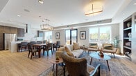 This thoughtfully designed single-floor community amenity space offers a seamless blend of functionality and modern style. The open-concept layout connects a fully equipped kitchen, multiple dining areas, and comfortable lounge spaces, all unified by warm wood-look flooring throughout.

The kitchen serves as a central hub, featuring a striking marble-topped island with seating, dark espresso cabinetry, stainless steel appliances, a subway tile backsplash, and a sleek overhead range hood — ideal for communal cooking and entertaining.

Adjacent to the kitchen, a spacious open lounge area draws the eye with a dramatic built-in fireplace framed by a chevron-patterned wood accent wall, flanked by custom shelving and topped with a wall-mounted television. Comfortable seating arrangements invite relaxed gathering, while natural light pours in through large windows and glass doors that open to an outdoor terrace with views of the surrounding area.

A dedicated dining area accommodates a large group table beneath a modern geometric chandelier, while a separate, more intimate dining room features rich navy textured walls and smaller grouped tables, offering a quieter setting for private gatherings.

Throughout, the space maintains a cohesive contemporary aesthetic with warm neutral tones, curated artwork, and thoughtful lighting that creates an inviting and versatile communal environment.