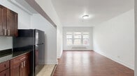 Located in Chicago's Woodlawn neighborhood along South Drexel Boulevard, this studio unit offers a practical and efficiently designed single-floor layout. The main living area combines the living room, dining space, and kitchen into one cohesive open-plan arrangement. Rich, warm hardwood-style flooring runs throughout the living space, complemented by crisp white walls and clean white baseboards that give the interior a bright, fresh feel. A bank of windows along the front wall allows natural light to fill the living area, with a baseboard heating unit positioned beneath them for year-round comfort. The kitchen is neatly defined within the open layout and features dark espresso-toned cabinetry with modern hardware, dark granite-style countertops, a stainless steel range, and a full-size refrigerator, all set over light tile flooring. A dedicated closet provides convenient storage, and an electrical panel is accessible within the unit. The bathroom is finished with floor-to-ceiling beige ceramic tile surrounding a full soaking tub and shower combination, and includes a window for natural ventilation. The overall design is clean and functional, making efficient use of the available space throughout.