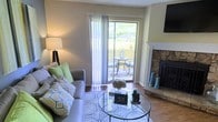 This single-floor residence offers a thoughtfully designed layout that balances comfort and functionality. The floor plan reveals multiple bedrooms, each with distinct character, along with well-defined living and transitional spaces connected by warm hardwood flooring throughout.

The living area serves as the heart of the home, anchored by a classic stone fireplace that adds texture and warmth to the room. A large sliding glass door floods the space with natural light and opens directly onto a private patio, where outdoor seating invites relaxation. The seamless indoor-outdoor connection enhances the overall sense of openness and livability.

The bedrooms are generously proportioned, with one featuring a calming blue-toned palette and another offering a bright, neutral aesthetic. Each room appears well-lit, contributing to an inviting ambiance throughout the residence.

A central hallway connects the various rooms efficiently, with a bathroom and additional utility spaces rounding out the functional core of the home. The overall design reflects a practical yet comfortable living environment, with consistent finishes and a cohesive style that ties each space together into a harmonious whole.