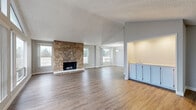 Located in Seattle's Meridian neighborhood, this single-floor, 3-bedroom, 2-bathroom residence offers a well-designed layout with a range of distinctive features. The expansive living room immediately impresses with soaring vaulted ceilings and a wall of large windows that flood the space with natural light and frame views of surrounding trees. A striking floor-to-ceiling stone fireplace serves as the room's focal point, anchoring the open feel of the space. Warm hardwood-style flooring runs throughout, creating a cohesive look across the living, dining, and kitchen areas. The galley-style kitchen is equipped with stainless steel appliances, rich wood cabinetry, and a built-in wet bar area with light blue cabinetry that connects seamlessly to the dining space. The generously sized primary bedroom features mirrored sliding closet doors, while secondary bedrooms offer ample space with accent walls and outdoor-facing windows. Two full bathrooms serve the home, including one with a tiled soaking tub and shower combination. Additional highlights include three closets, a dedicated laundry room with overhead cabinetry, and a private sauna — a rare and desirable amenity. The textured ceilings and neutral gray tones throughout lend the home a clean, timeless character.