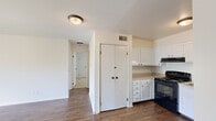 This single-floor, 2-bedroom, 1-bathroom unit offers an efficiently designed layout that makes practical use of its compact footprint. The living room is a bright, open space anchored by dark hardwood-style flooring and a sliding glass door that floods the room with natural light while providing direct access to an outdoor balcony with greenery views. The layout connects the living area seamlessly to the kitchen, which is equipped with white shaker-style cabinetry, light countertops, and a full suite of black appliances including a gas range, dishwasher, and refrigerator. A built-in pantry with double doors adds notable storage. A hallway leads to the two bedrooms, both finished with neutral carpet. The primary bedroom offers a comfortable footprint with a closet and a window overlooking outdoor greenery. The second bedroom is similarly carpeted with a closet and natural light from a window. The full bathroom features a clean, white tub-shower combination with chrome fixtures. Neutral walls throughout maintain a cohesive and understated aesthetic.