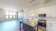 Located in the vibrant Logan Square neighborhood of Chicago, this single-floor unit at 2522 N Milwaukee Ave offers a thoughtfully designed, modern living space. The open-concept kitchen is a standout feature, showcasing floor-to-ceiling white cabinetry, a textured tile backsplash, a center island with a gray countertop and built-in shelving, and a full suite of stainless steel appliances including a gas range, microwave, dishwasher, and refrigerator. Track lighting overhead adds a contemporary touch. Light wood-style flooring runs throughout, connecting the kitchen seamlessly to the open living area, which benefits from large windows that invite abundant natural light and views of the surrounding neighborhood. A striking accent wall in teal adds a bold design element to the living space. The unit includes two bathrooms: one featuring a dual-sink vanity with wood cabinetry, a white quartz countertop, and a tiled soaking tub with shower combination; the other offering a single-sink vanity and a glass-enclosed walk-in shower with stone tile surround. The bedroom is bright and airy, with a large window framing city views. A well-organized walk-in closet with built-in shelving and hanging rods provides ample storage throughout.
