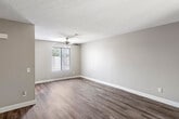 Located at 1313 W Memory Ln in Santa Ana, California, this single-floor residence offers a straightforward and functional layout across its living spaces. The main living area is generously sized, featuring rich dark wood-look flooring, neutral beige walls, crisp white baseboards, and a textured ceiling. A ceiling fan provides year-round comfort, while a large front-facing window allows natural light to fill the room and offers views of the surrounding greenery. An entry area with its own window continues the same flooring and light-toned palette, creating a welcoming transition into the home. The bedrooms are carpeted for added comfort, with neutral walls and windows that bring in natural light and outdoor views. One bedroom features a full wall of mirrored sliding closet doors, enhancing the sense of space. The bathroom is clean and well-appointed, offering a large wall mirror, a single vanity with brushed nickel fixtures, and a tub-shower combination. The kitchen is equipped with warm wood cabinetry, white countertops, a stainless steel sink positioned beneath a window overlooking palm trees, and space for appliances. Throughout the home, a consistent neutral color scheme contributes to a calm and cohesive atmosphere.